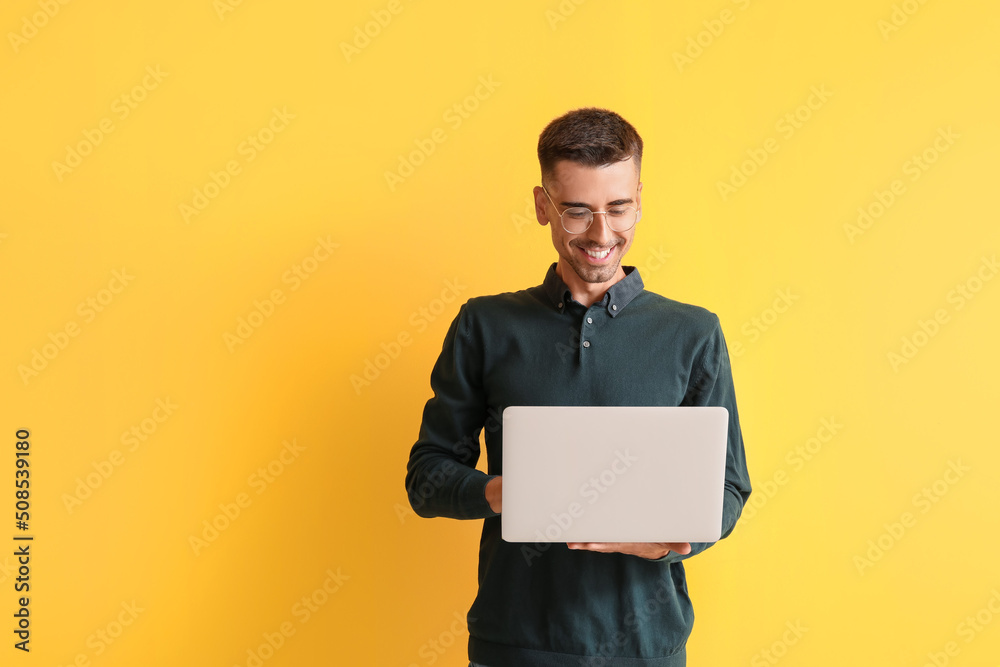 Handsome man in eyeglasses using laptop on yellow background Handsome man in eyeglasses using laptop on yellow background