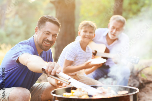 Handsome man cooking food on grill with his family at barbecue party