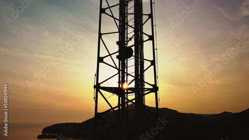 Amazing closeup sunset drone view of silhouette of cell tower. Wireless connection. Spectacular view of cellular tower with mountains and sea in the background. 5G network. Сell site