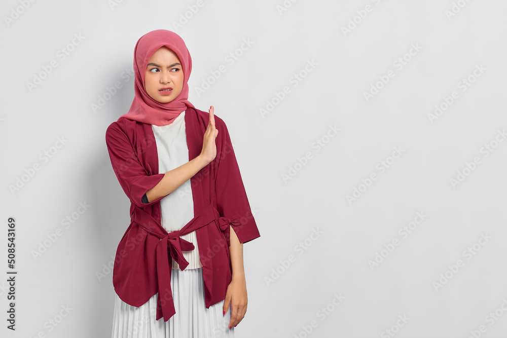 Displeased beautiful Asian woman in casual shirt showing stop gesture, saying no, expressing rejection isolated over white background