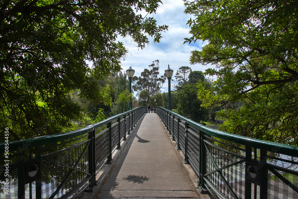 Bridge with lanterns in a city park surrounded by green trees, cityscape