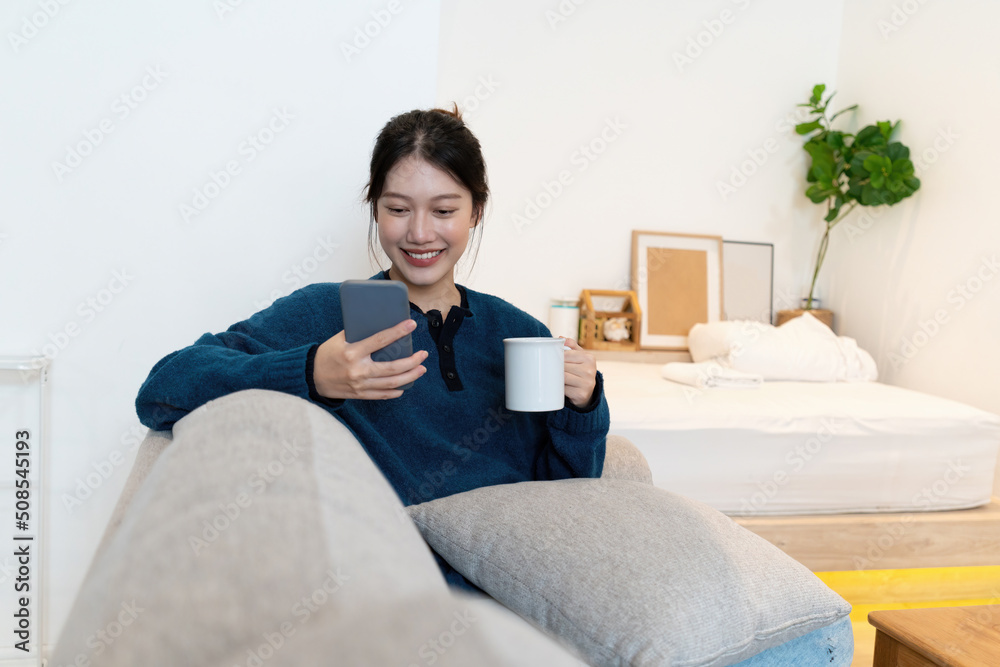 Portrait of Young Asian woman chatting with her friend and checking social media by smartphone sitting on couch. Lifestyle concept. Portrait of Young Asian woman chatting with her friend and checking social media by smartphone sitting on couch. Lifestyle concept.