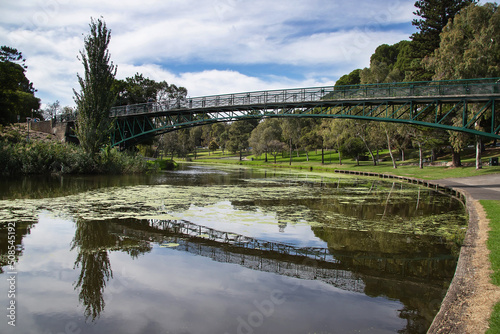 Bridge over the river in the city park surrounded by green trees with reflection in the water  cityscape