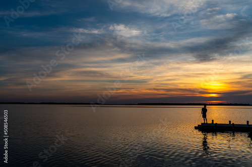 Sun Sitting behind Boy Fishing at Dock