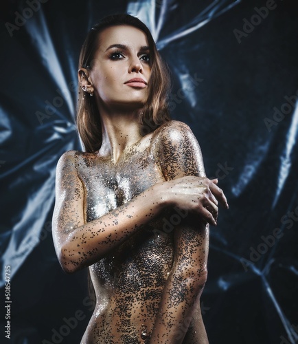 High Fashion model girl with bright golden sparkles on her body posing, full length portrait of beautiful sexy woman with glowing body skin. Art design make up. Glitter gold sequins on skin body art