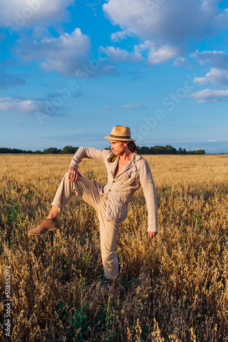 Tall handsome man dressed in a coarse linen suit and hat standing in a strange pose at golden oat field