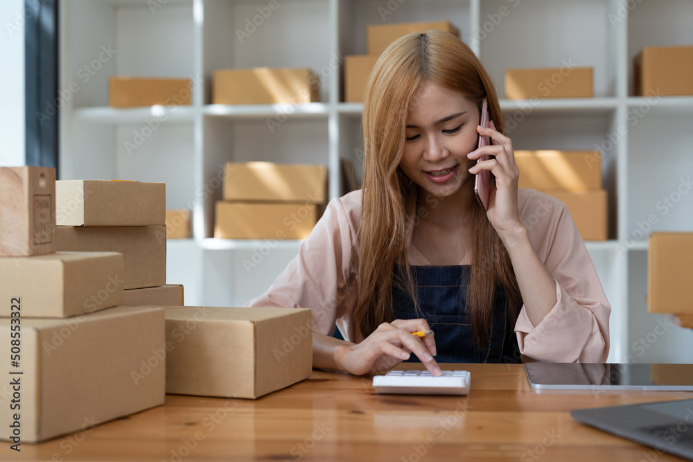 Drop shipping business owner talking on mobile phone and taking order. Female entrepreneur working at home office confirming the order on phone. Drop shipping business owner talking on mobile phone and taking order. Female entrepreneur working at home office confirming the order on phone.