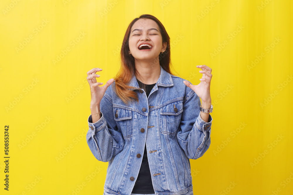 Stressed asian woman standing while shouting and closing her eyes. Isolated on yellow background Stressed asian woman standing while shouting and closing her eyes. Isolated on yellow background