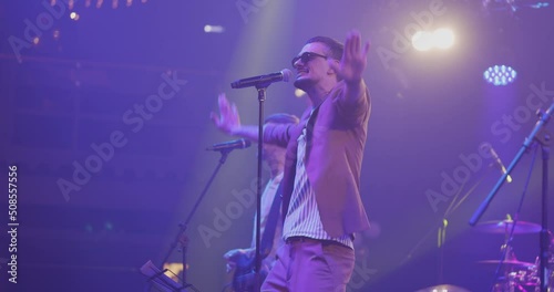 Men singing to microphone on light background. Stylish cool guy performing concert on stage. Music and concert concept.