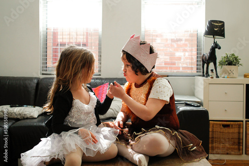 Two girls dressed as princesses playing together inside