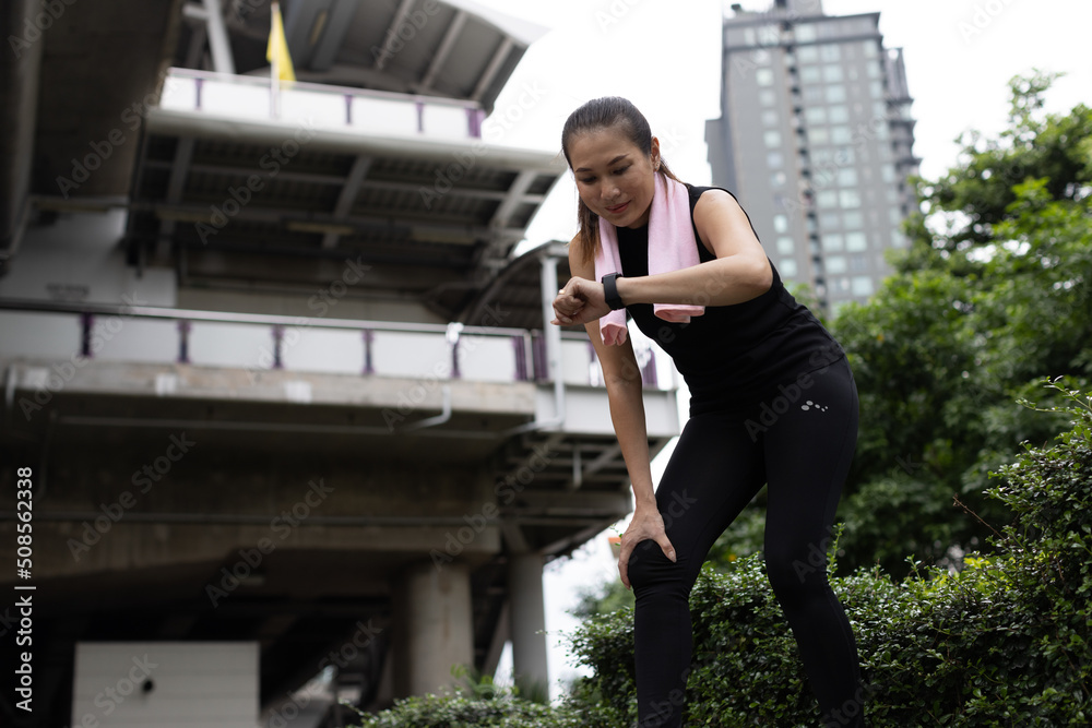 Asian women in sportswear stop and looking to screen of fitness application in smartwatch on wrist to check results after workout or exercise. Concept of good health care