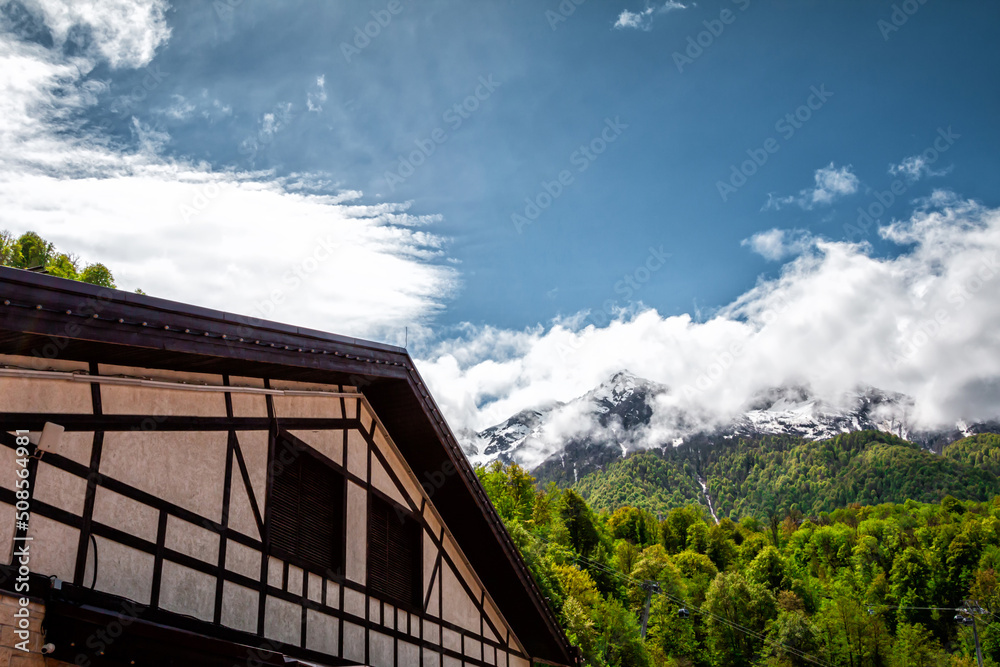 Half-timbered house against the backdrop of a green forest and high snow-capped mountains