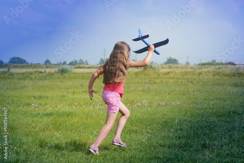 A girl runs through a green field with a toy airplane in her hands