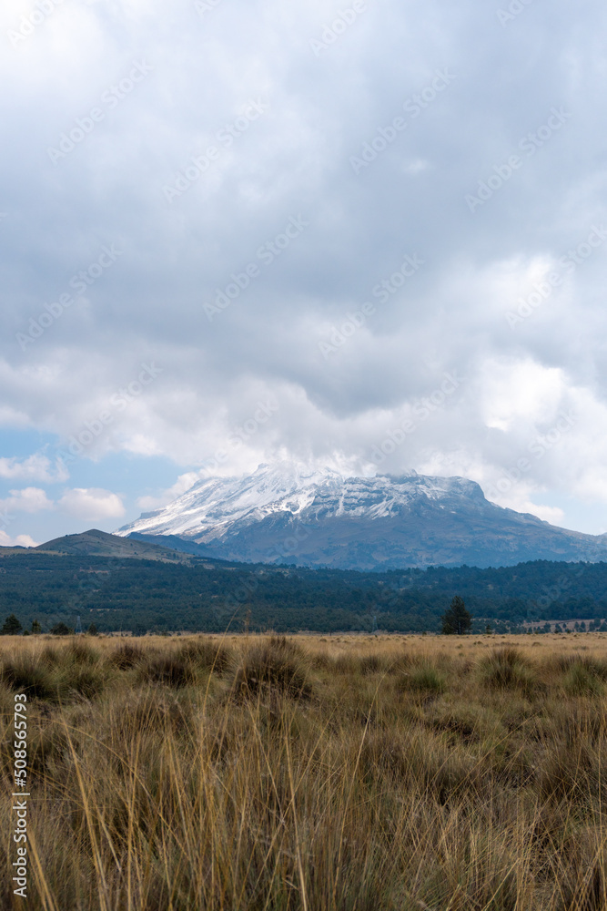 Iztaccihuatl volcano covered with snow and surrounding valley with yellow grass
