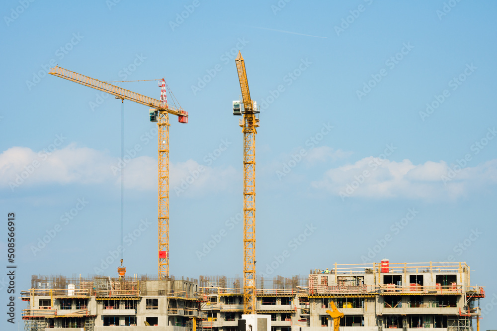 Two large yellow industrial cranes operating on an apartment house construction site Two large yellow industrial cranes operating on an apartment house construction site