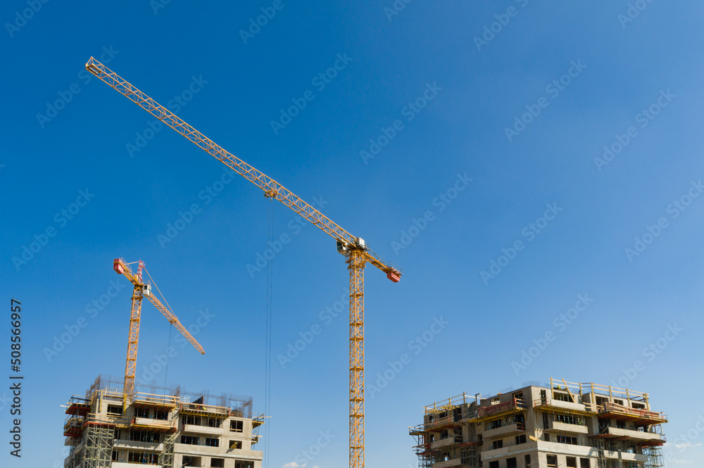 Two large yellow industrial cranes operating on an apartment house construction site Two large yellow industrial cranes operating on an apartment house construction site