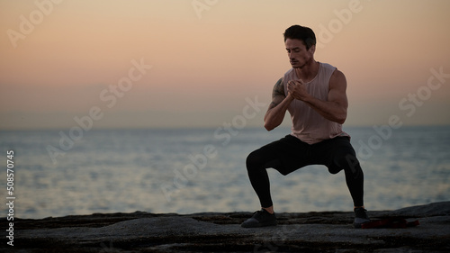 Male doing stretch exercise beside ocean