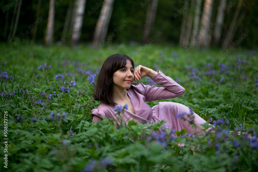 A beautiful girl walks in the forest. Field of blue flowers. Girl in a pink dress. Brunette. A beautiful girl walks in the forest. Field of blue flowers. Girl in a pink dress. Brunette.