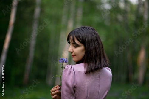 A beautiful girl walks in the forest. Field of blue flowers. Girl in a pink dress. Brunette.