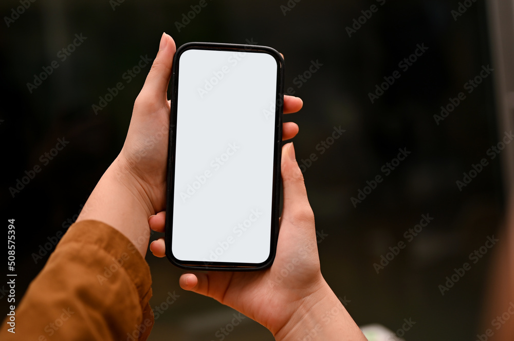 A smartphone or cellphone mockup is in a woman's hands over blurred dark background.