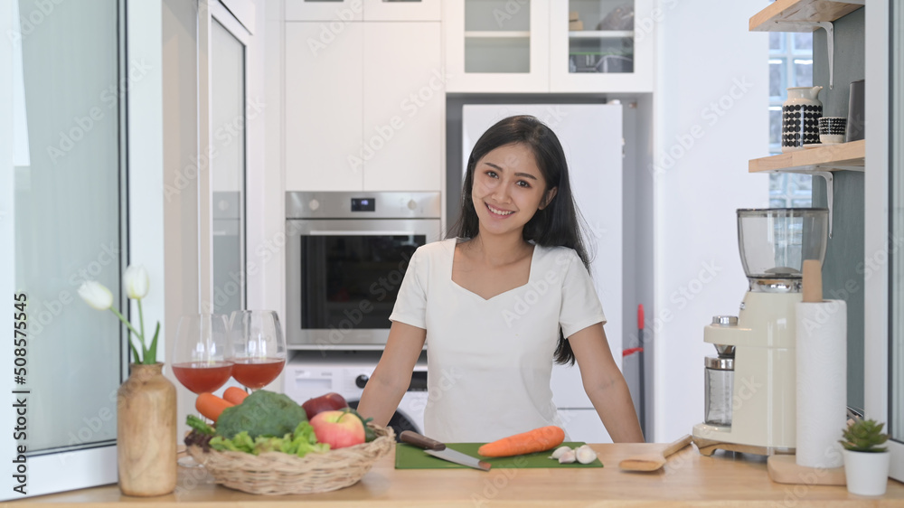 Healthy young woman standing at kitchen counter and preparing ingredients for making vegetarian food