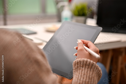 Close-up shot of a millennial woman in comfy sweater using tablet touchpad