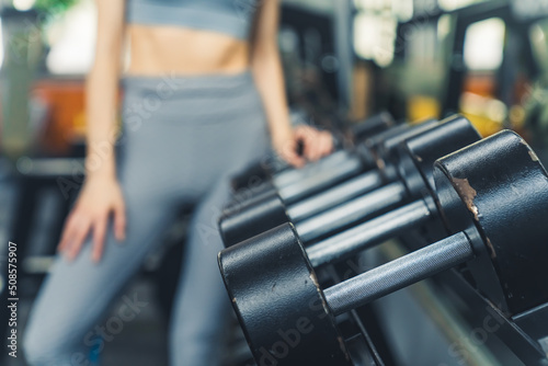 Close up of a blurred caucasian woman selecting one of black dumbbell weight at gym. Healthy lifestyle concept. High quality photo