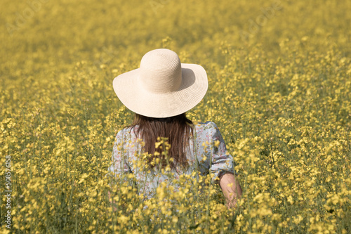 woman in blue dress with sun hat standing in field 0f yellow wild flowers in summer photo