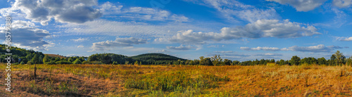 panorama  beautiful view from the field to the hilly area with clouds on the blue sky