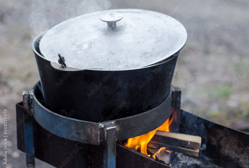 large camp pot over fire. Pot for cooking over fire. Fire made in grill. large camp pot over fire. Pot for cooking over fire. Fire made in grill.