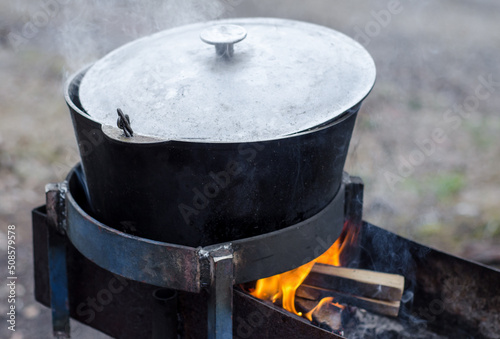 large camp pot over fire. Pot for cooking over fire. Fire made in grill. 