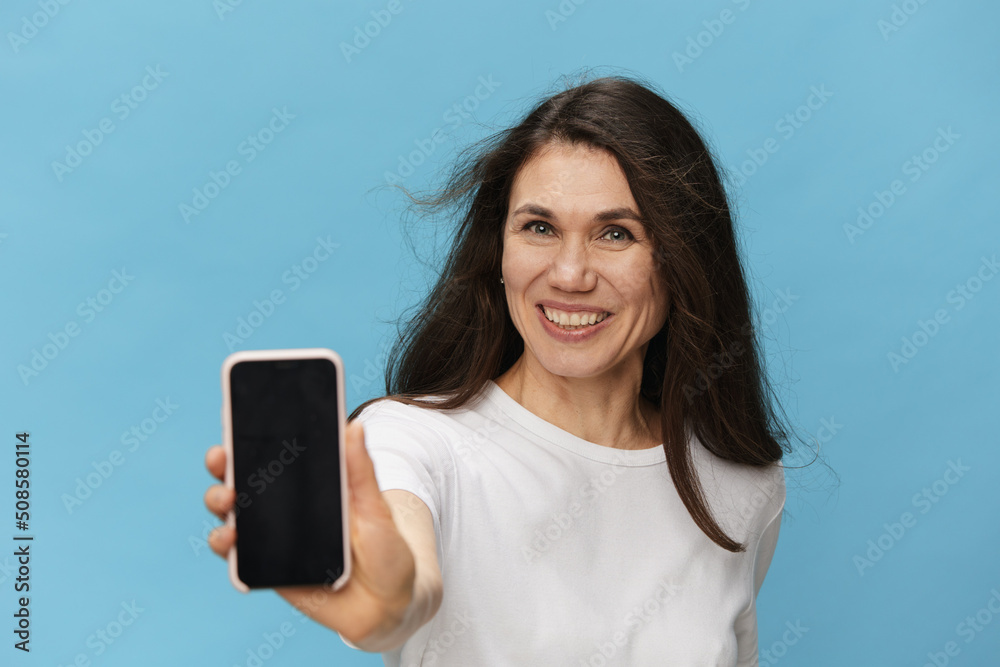 beautiful happy woman with hair blowing in the wind smiles showing the phone to the camera.