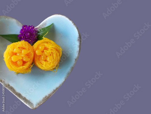 Top view Close up of Thai style Fios de ovos, rolled golden egg yolk thread, traditional sweet food dessert in blue heart shape plate, copy space with clipping path