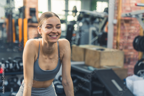 Medium indoor shot at a gym. Joyful fulfilled european woman in her 20s in a sports bra and leggings looking ahead and smiling after a training. High quality photo
