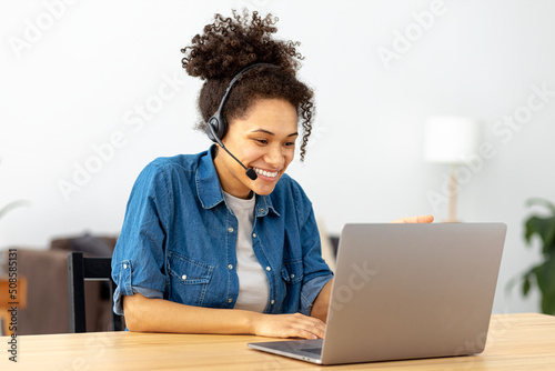 Obraz na płótnie Successful African American woman in headset, office employee or call center worker sitting in a modern office talking, consulting client using video call, smile w salonie