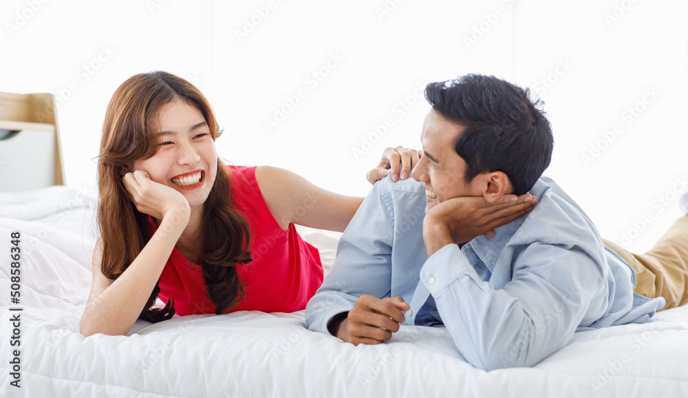 Asian young romantic lover couple boyfriend and girlfriend in casual outfit laying down smiling together on bed while male using hand touching and sleeking adjusting female hair in bedroom at home. Asian young romantic lover couple boyfriend and girlfriend in casual outfit laying down smiling together on bed while male using hand touching and sleeking adjusting female hair in bedroom at home.