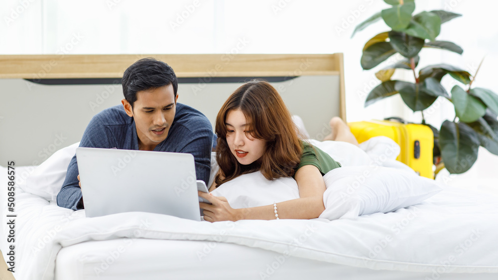 Fototapeta premium Asian upset stressed depressed frowning face male female husband and wife couple lay down together on pillow under blanket on bed having debt problem making payment shopping online via credit card