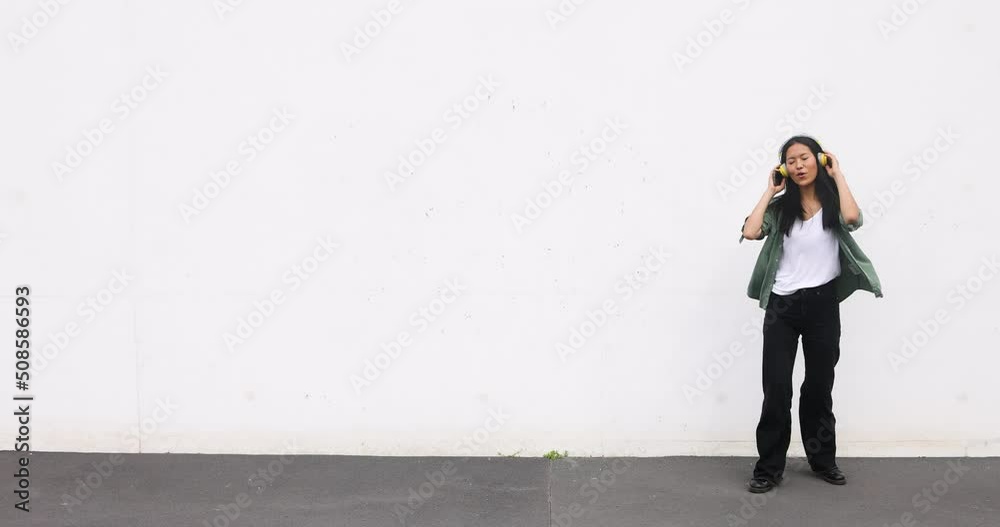 Young woman with headphones dancing and jumping in front of white wall Young woman with headphones dancing and jumping in front of white wall