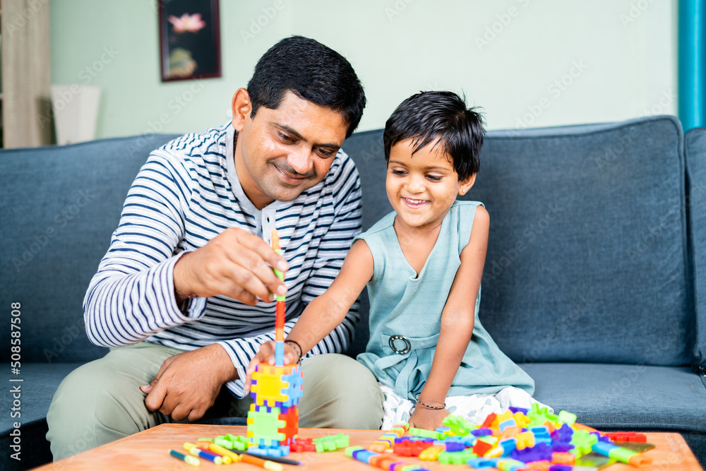 Father helping little daughter to make or build toy at home - concept of spending family time, childhood growth and development Father helping little daughter to make or build toy at home - concept of spending family time, childhood growth and development