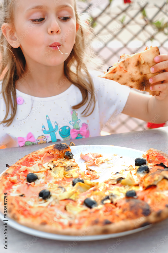 Hungry kid girl eating pizza on cafe terrace on sunny day. outside restaurant.Vertical.