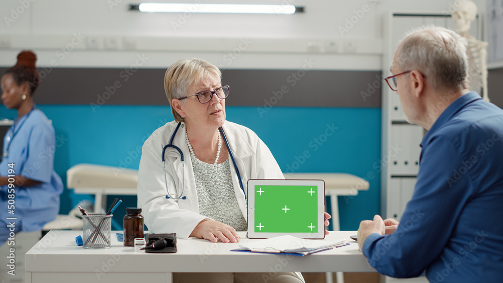 General practitioner analyzing horizontal greenscreen on digital tablet with retired patient in cabinet. Blank mockup template with isolated chroma key and copyspace background on gadget.