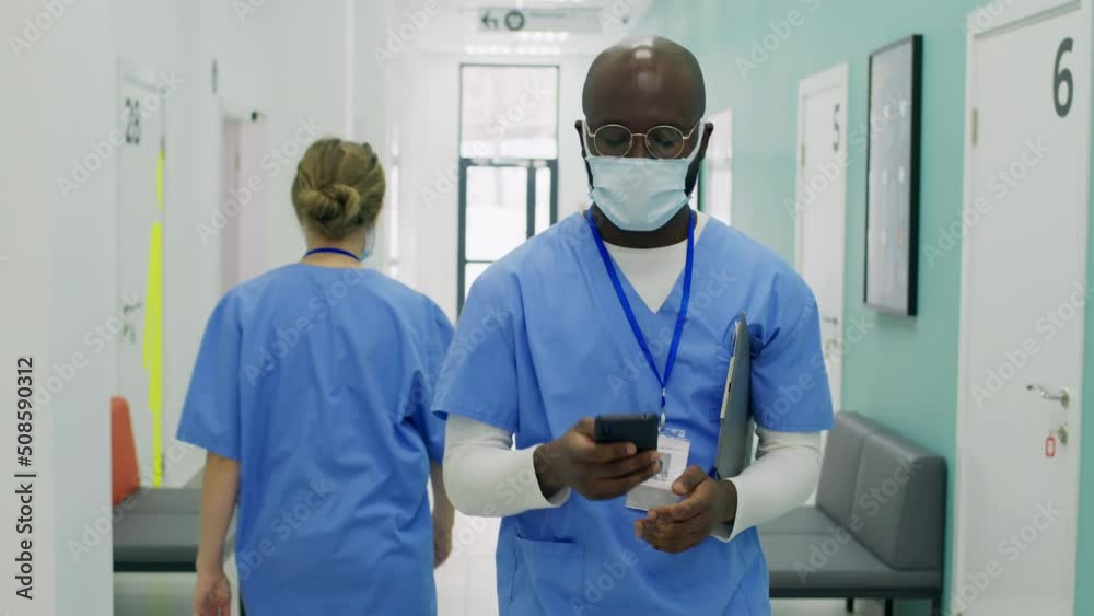 Male nurse with surgical mask walking in hospital using smartphone