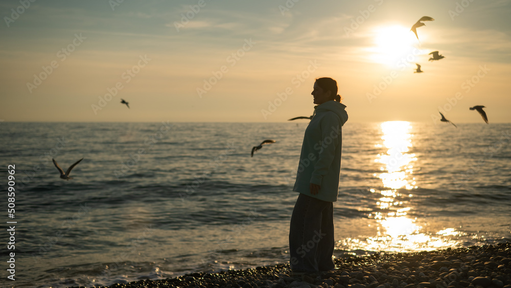 Caucasian woman feeding seagulls at sunset by the sea. 