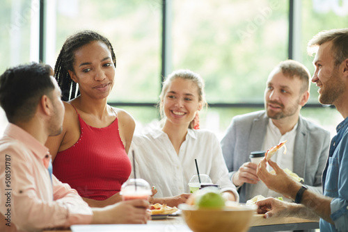 Pretty African student in red top standing at high table and having lunch while meeting European friends