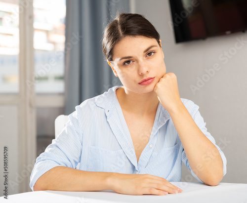 Portrait of single upset young woman sitting at table in cozy home interior