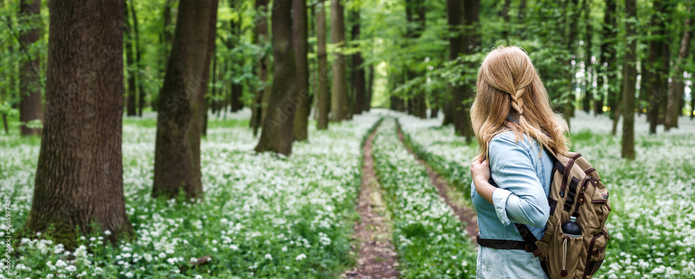 Tourist woman with backpack hiking on footpath in forest at spring ...