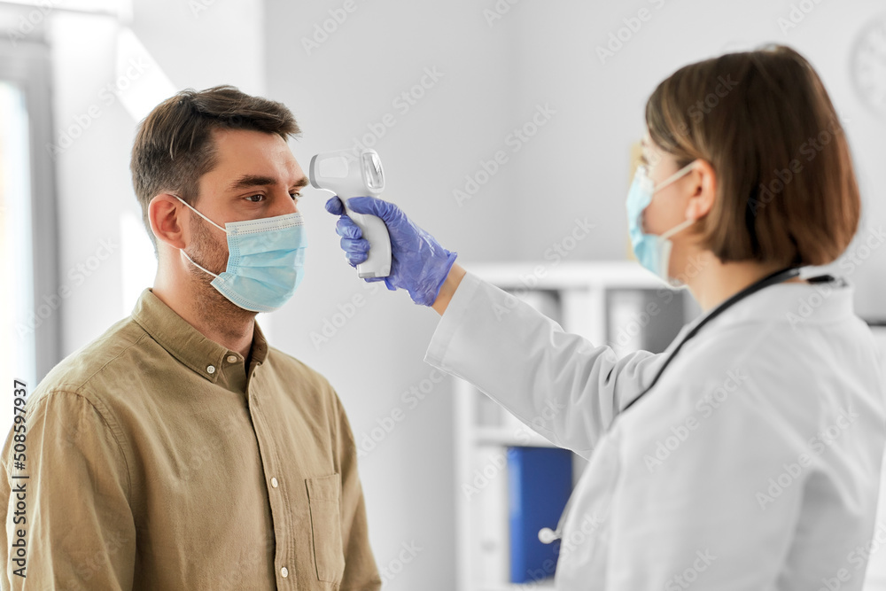 medicine, healthcare and people concept - female doctor in mask with infrared forehead thermometer measuring temperature of man patient at hospital medicine, healthcare and people concept - female doctor in mask with infrared forehead thermometer measuring temperature of man patient at hospital
