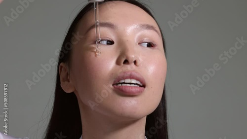 Young asian girl applying cosmetology serosity on her skin. Pipette of serum in girl's hand. Cosmetogy procedure. Portrait isolated. Oil on skin