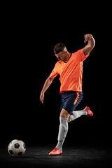 Studio shot of professional male football soccer player in motion isolated on dark background. Concept of sport, goals, competition, hobby, achievements