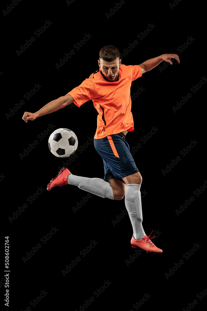 Studio shot of professional male football soccer player in motion isolated on dark background. Concept of sport, goals, competition, hobby, achievements
